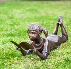 Bronzefigur "liegendes Mädchen mit Buch" . Bronzefiguren und Gartenfiguren bei Kunsthandel Lohmann in Timmendorfer Strand.